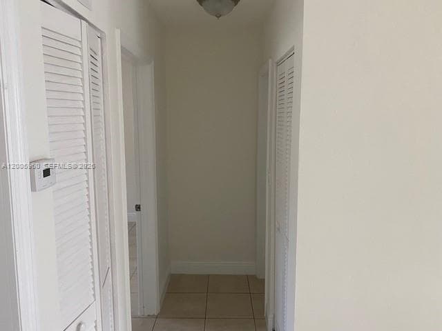 Hallway featuring neutral-toned tile flooring, two louvered-door closets, and a flush-mount ceiling light fixture