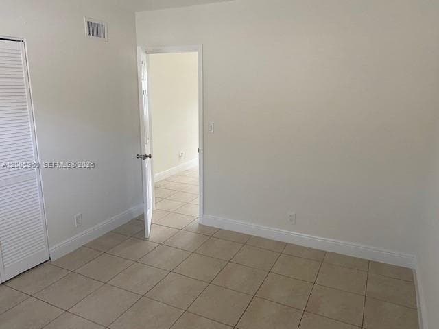 Neutral-toned ceramic tile flooring, solid-panel interior door with brushed metal hardware, and louvered closet doors