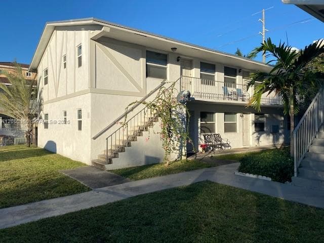 Two-story exterior featuring light-colored stucco siding with decorative timber detailing, an upper-level balcony with metal railing, and an external concrete staircase