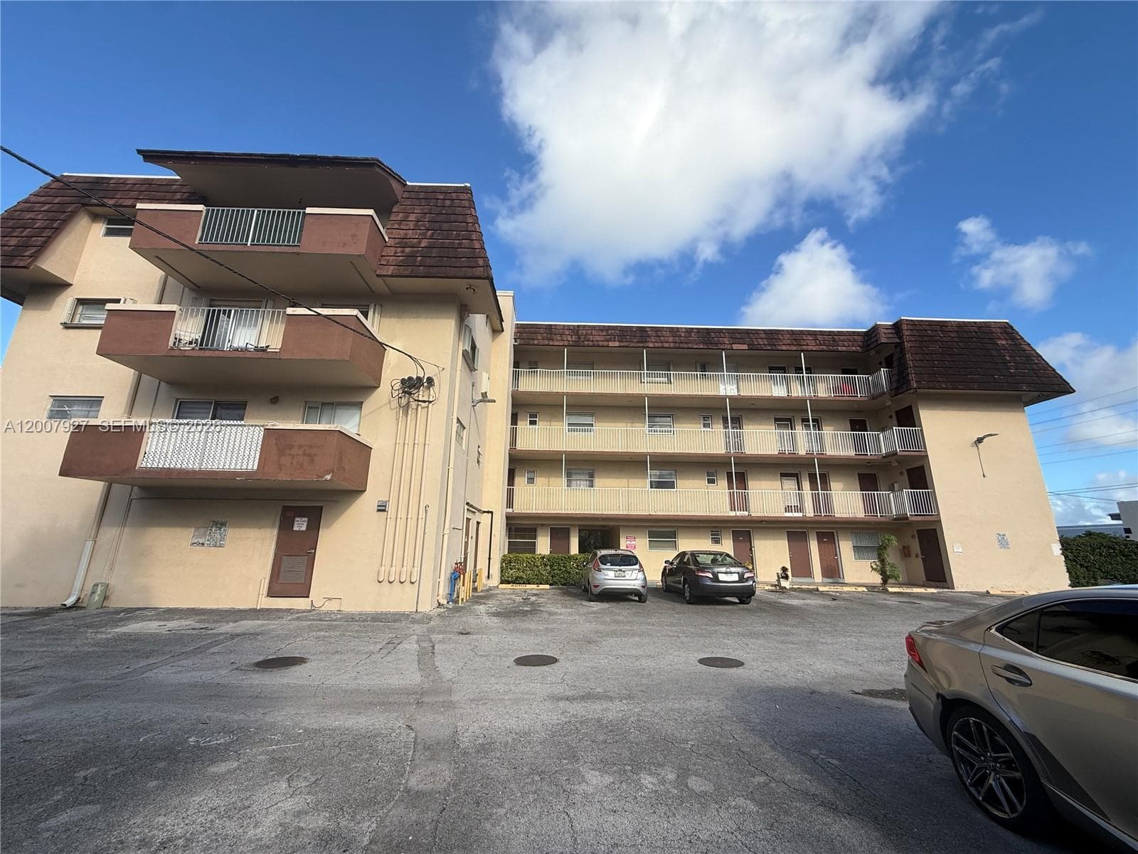 Multi-story residential building exterior featuring stucco siding, textured roof shingles, and private balconies with metal railings