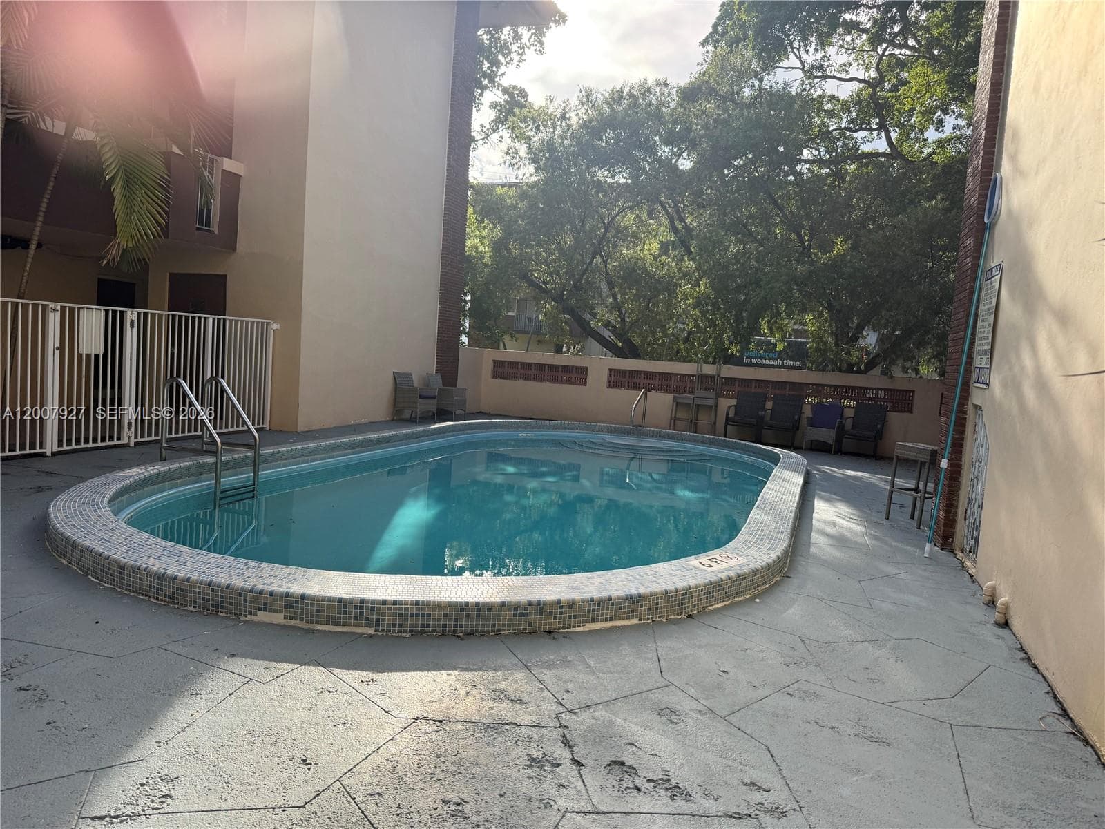 Oval swimming pool featuring a mosaic tile border, metal pool ladder, and concrete patio surround