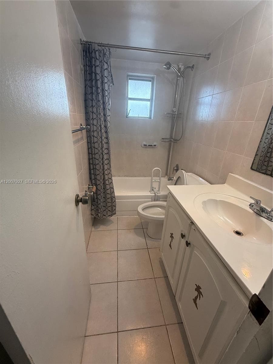 Bathroom featuring a vanity with an integrated sink, porcelain tile flooring, tile-surround bathtub, and an adjustable-height shower fixture