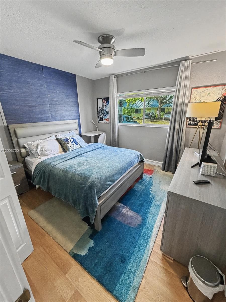 Spacious second bedroom with stylish accent wall, ceiling fan, and natural light