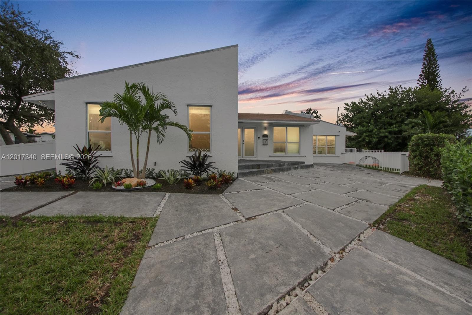Modern exterior featuring a geometric roofline, white stucco finish, large-format paver driveway with crushed stone accents, and manicured landscaping