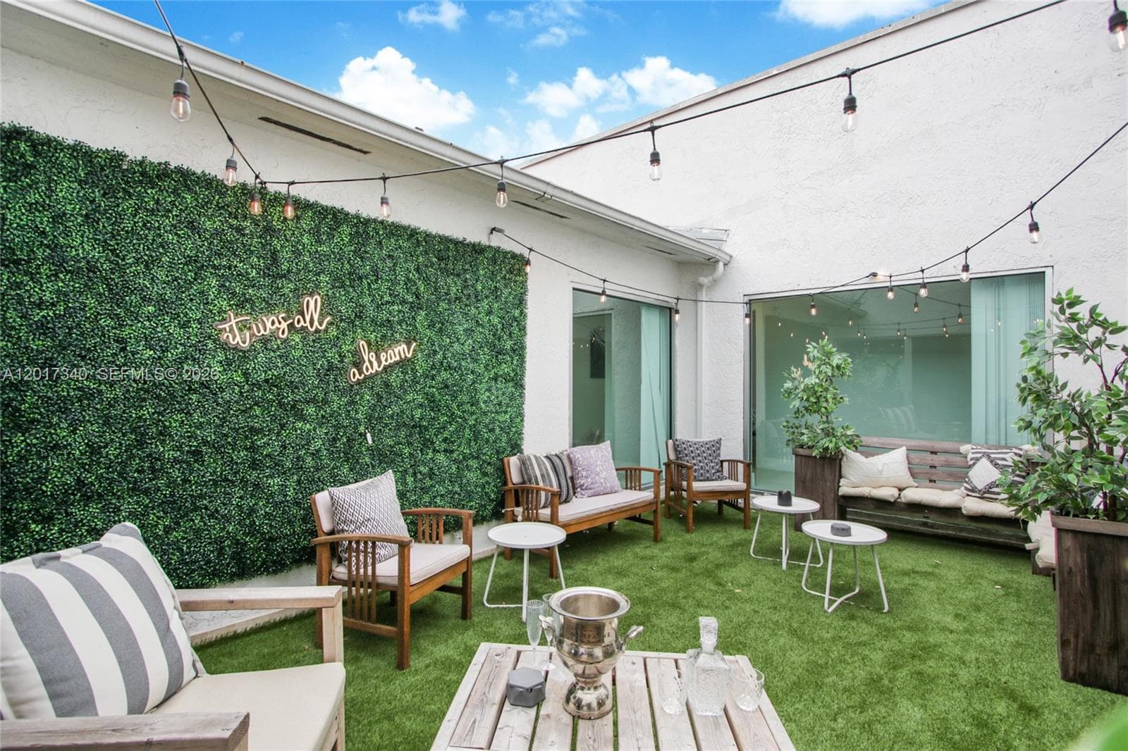 Private courtyard featuring synthetic turf, artificial hedge wall, and exterior string lighting