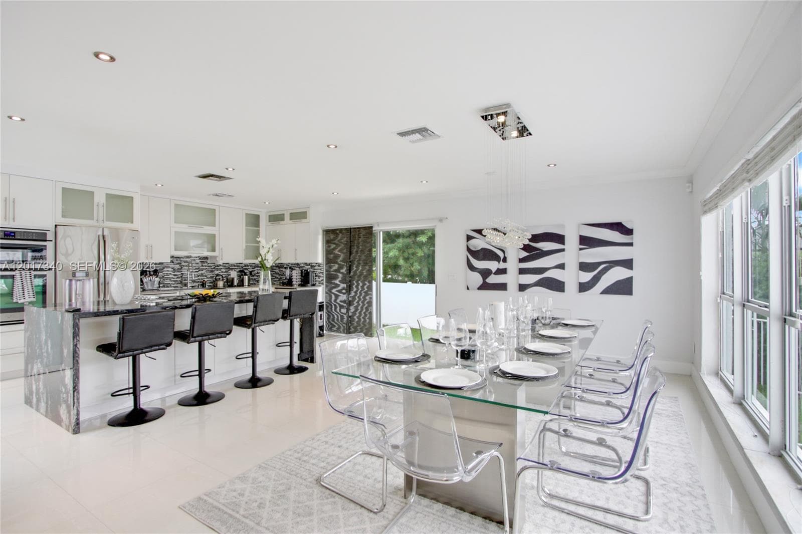Open-concept kitchen featuring white shaker cabinetry, stone-surfaced center island with waterfall edge, patterned tile backsplash, recessed ceiling lighting, and large-format tile flooring