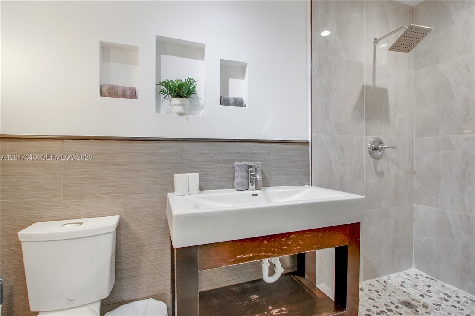 Bathroom featuring a wood-finish vanity with a white vessel sink, three recessed wall niches, and a walk-in shower with large-format wall tile and stone-finish flooring