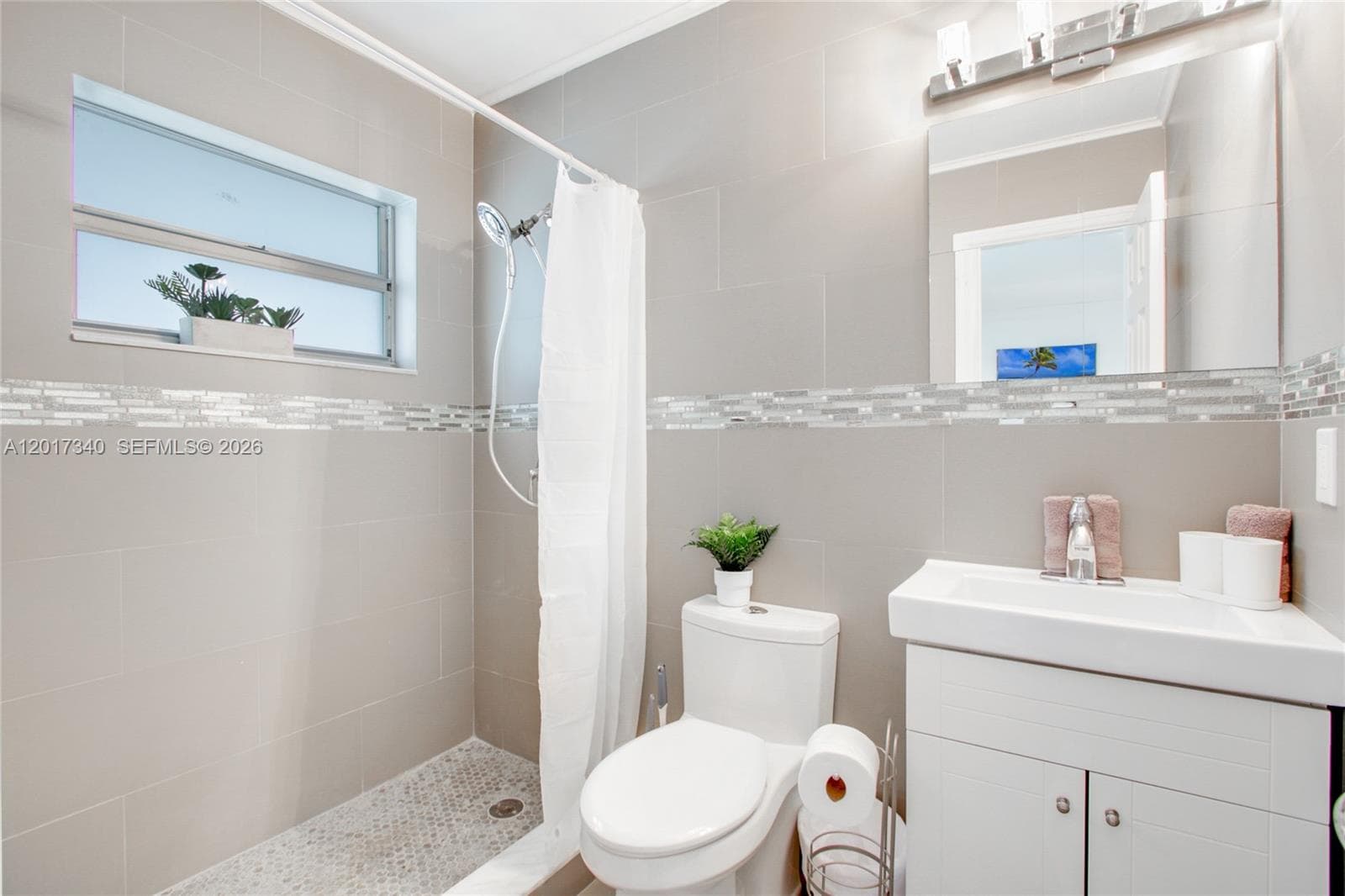 Bathroom featuring large-format wall tile, glass-tiled inlay, a walk-in shower with pebble-finish flooring, a vanity with an integrated basin, and an attached wall mirror