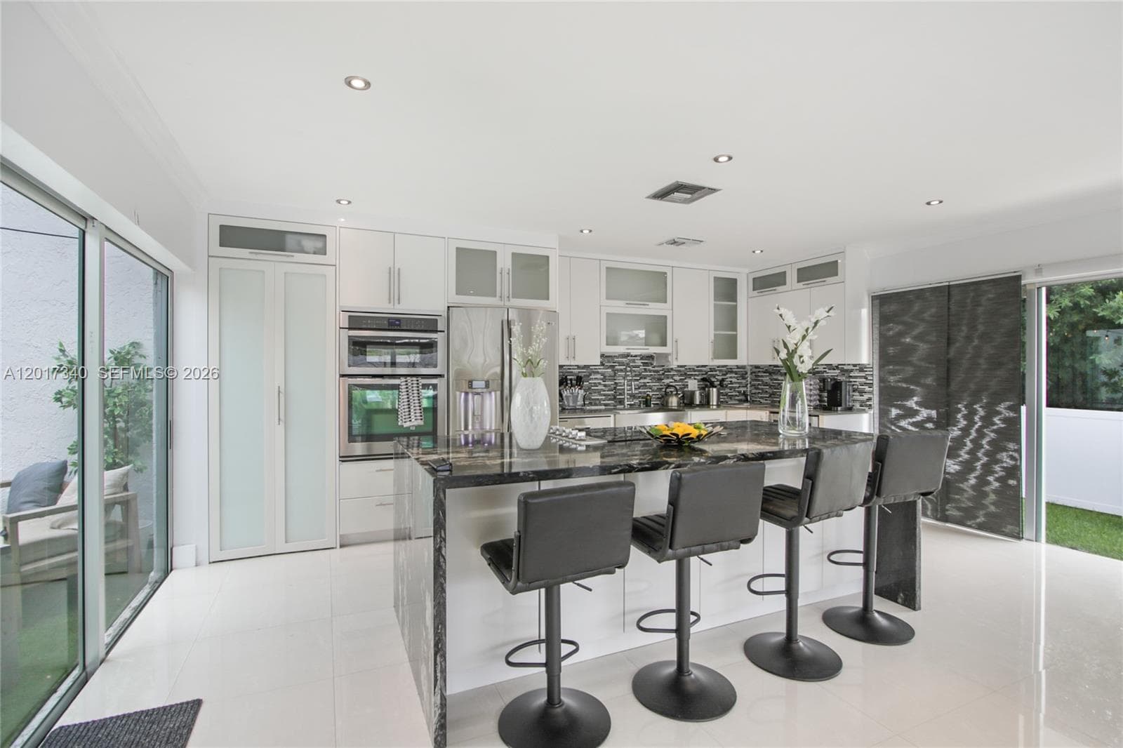 Kitchen featuring white cabinetry with glass-panel accents, a stone-topped island, a built-in wall oven, a mosaic tile backsplash, and large-format floor tiling