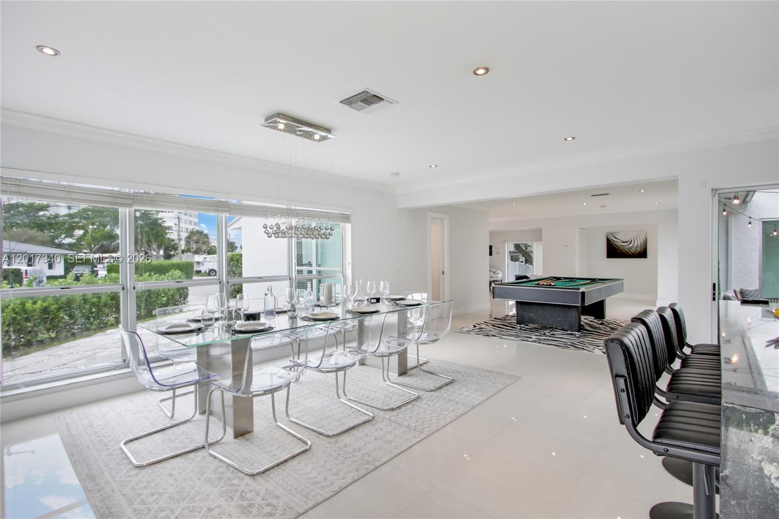 Open-concept interior featuring large-format polished tile flooring, recessed lighting, crown molding, a decorative multi-light chandelier, and floor-to-ceiling windows