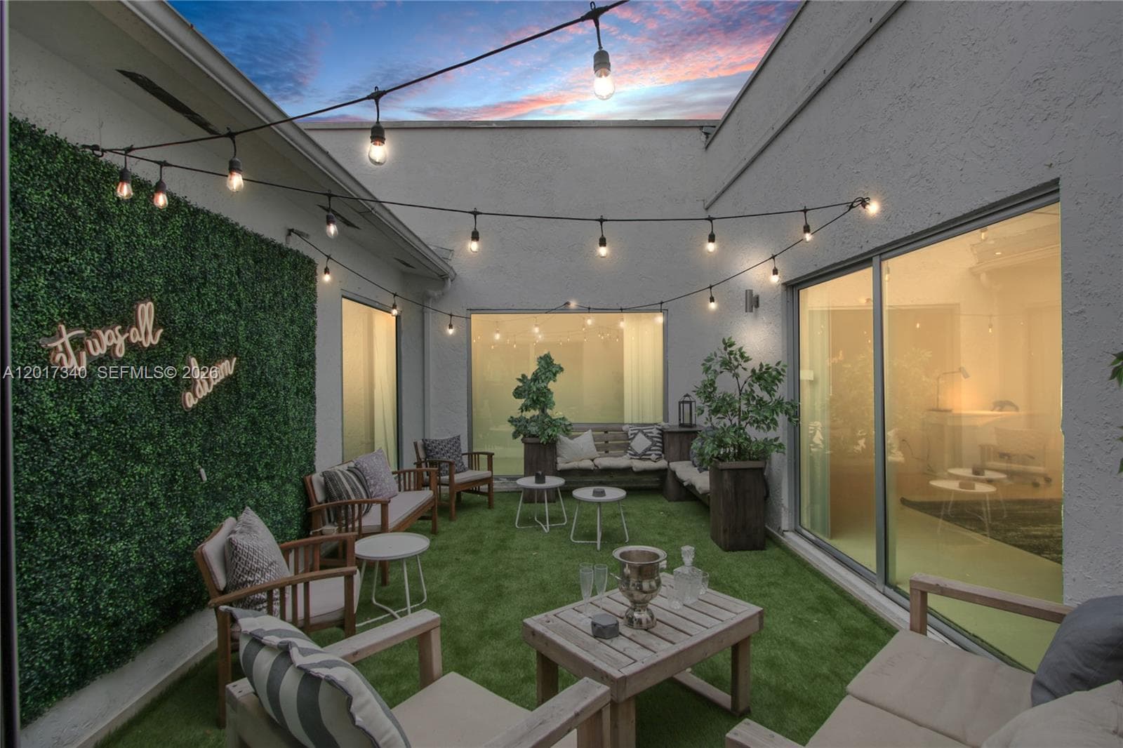 Enclosed courtyard featuring artificial turf, textured exterior walls, integrated string lighting, and large sliding glass doors