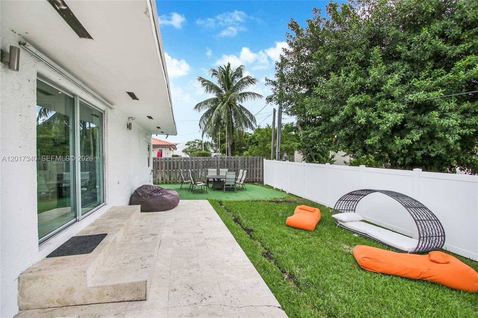 Backyard featuring a paved stone patio, manicured lawn, white vinyl perimeter fencing, and sliding glass exterior doors