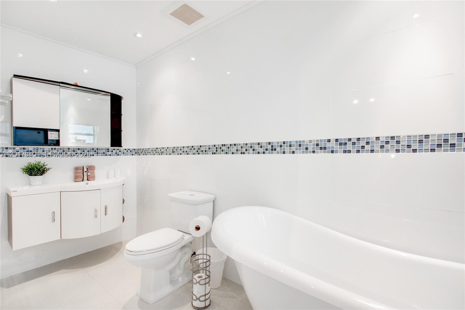Freestanding soaking tub, wall-mounted floating vanity with integrated sink, recessed lighting, and glass mosaic tile backsplash