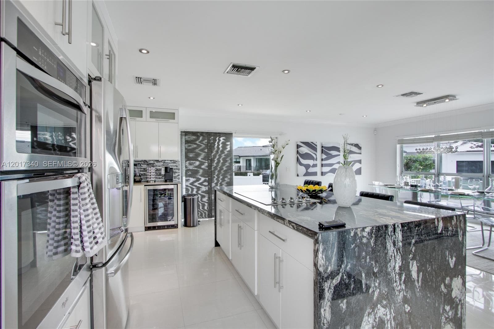 Kitchen featuring white flat-panel cabinetry, a central island with a waterfall-edge stone countertop, stainless steel double wall ovens, a built-in wine refrigerator, and recessed lighting