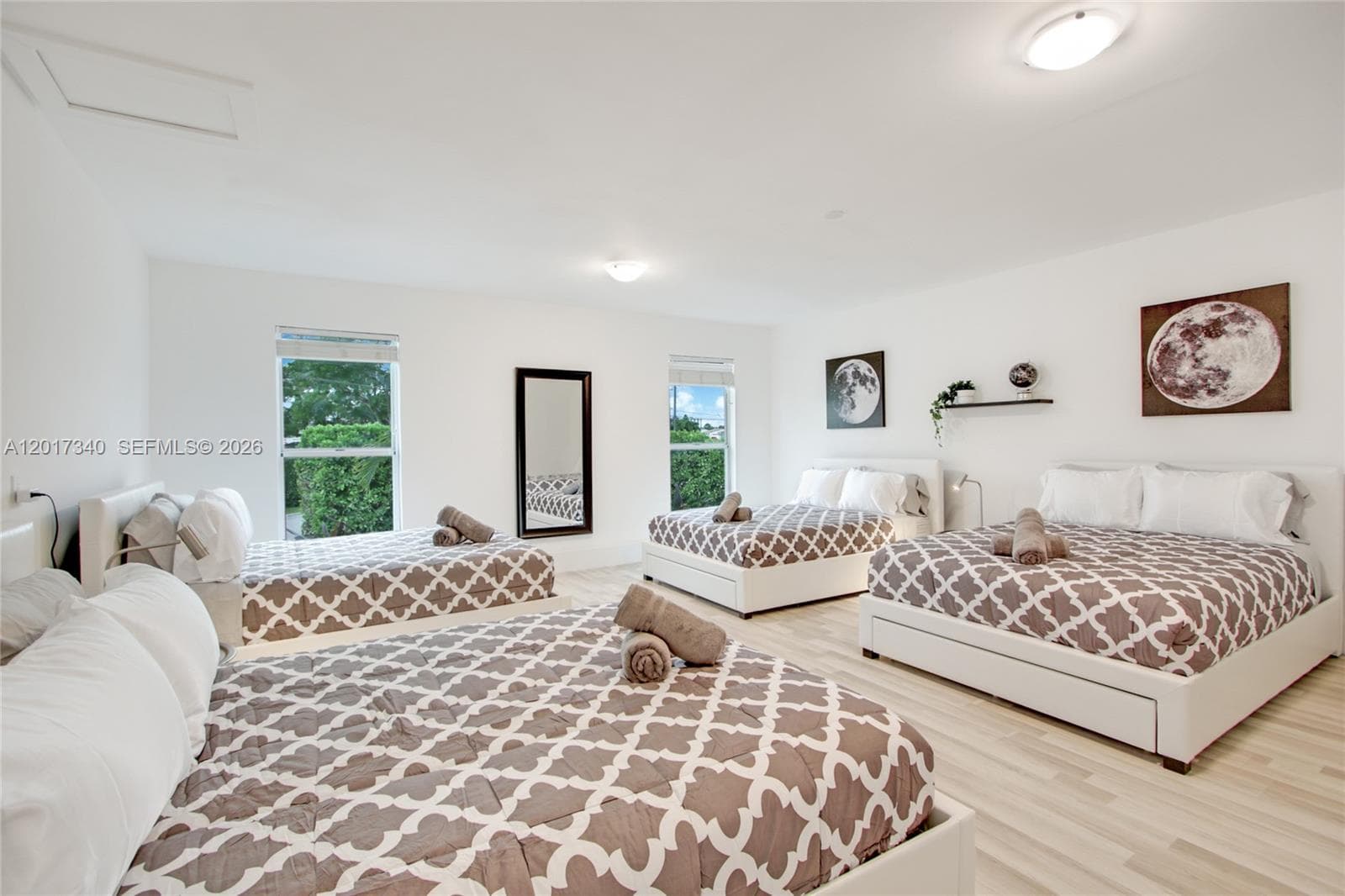 Spacious room featuring light-toned wood-finish flooring, crisp white walls, flush-mount ceiling lighting, and multiple windows providing natural illumination