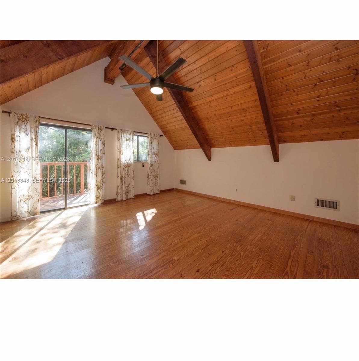Vaulted ceiling with exposed wood beams and wood-plank paneling, wood-finish flooring, and sliding glass doors with access to an exterior deck