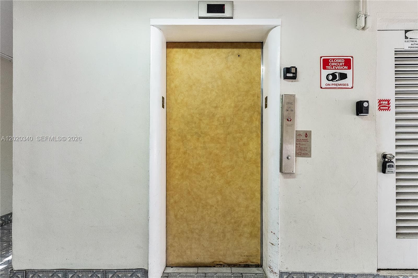 A vintage elevator with a gold-toned door, keypad access, and CCTV signage — functional and secure, with that classic older Florida building character.