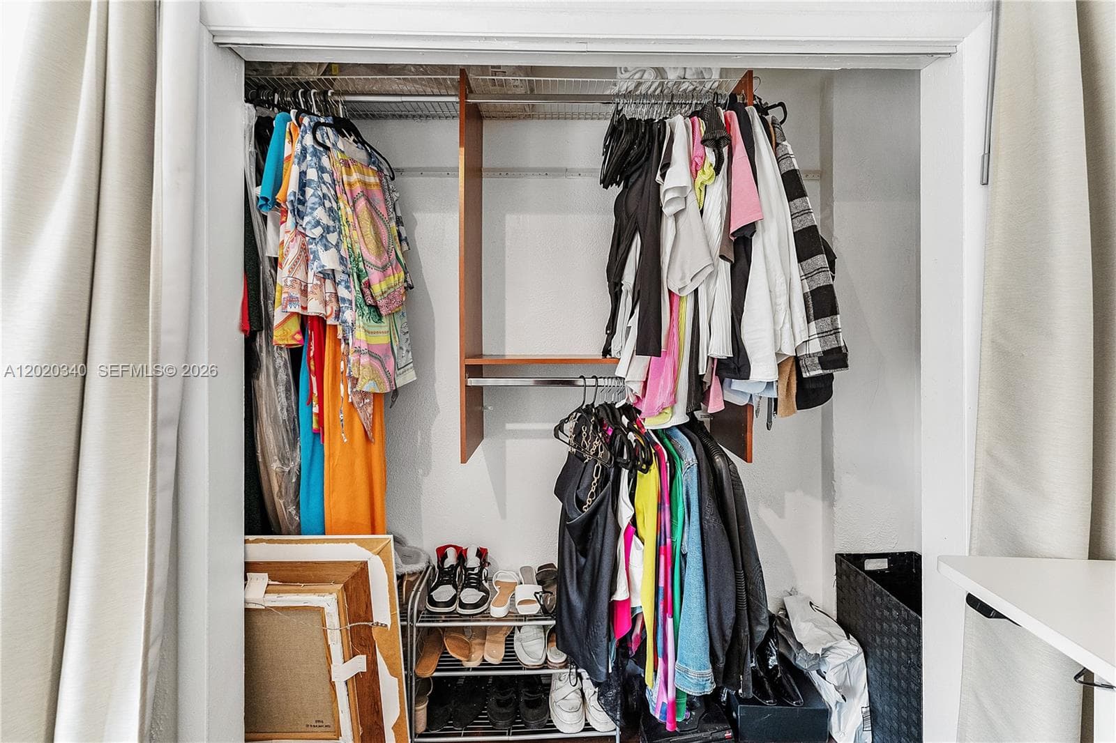 A spacious reach-in closet with double hanging rods, packed with colorful clothing and a shoe rack below. Functional and well-used, with room to organize further.