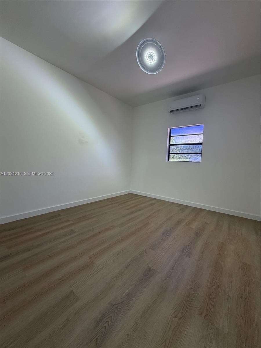 Interior space featuring wood-finish flooring, a wall-mounted ductless mini-split air conditioning unit, and a louvered window