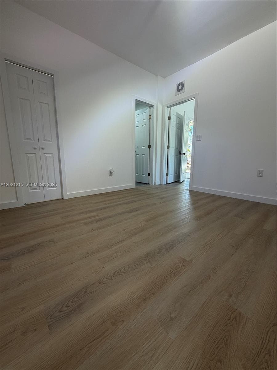 Interior room featuring wood-finish flooring, white walls, and three paneled closet doors