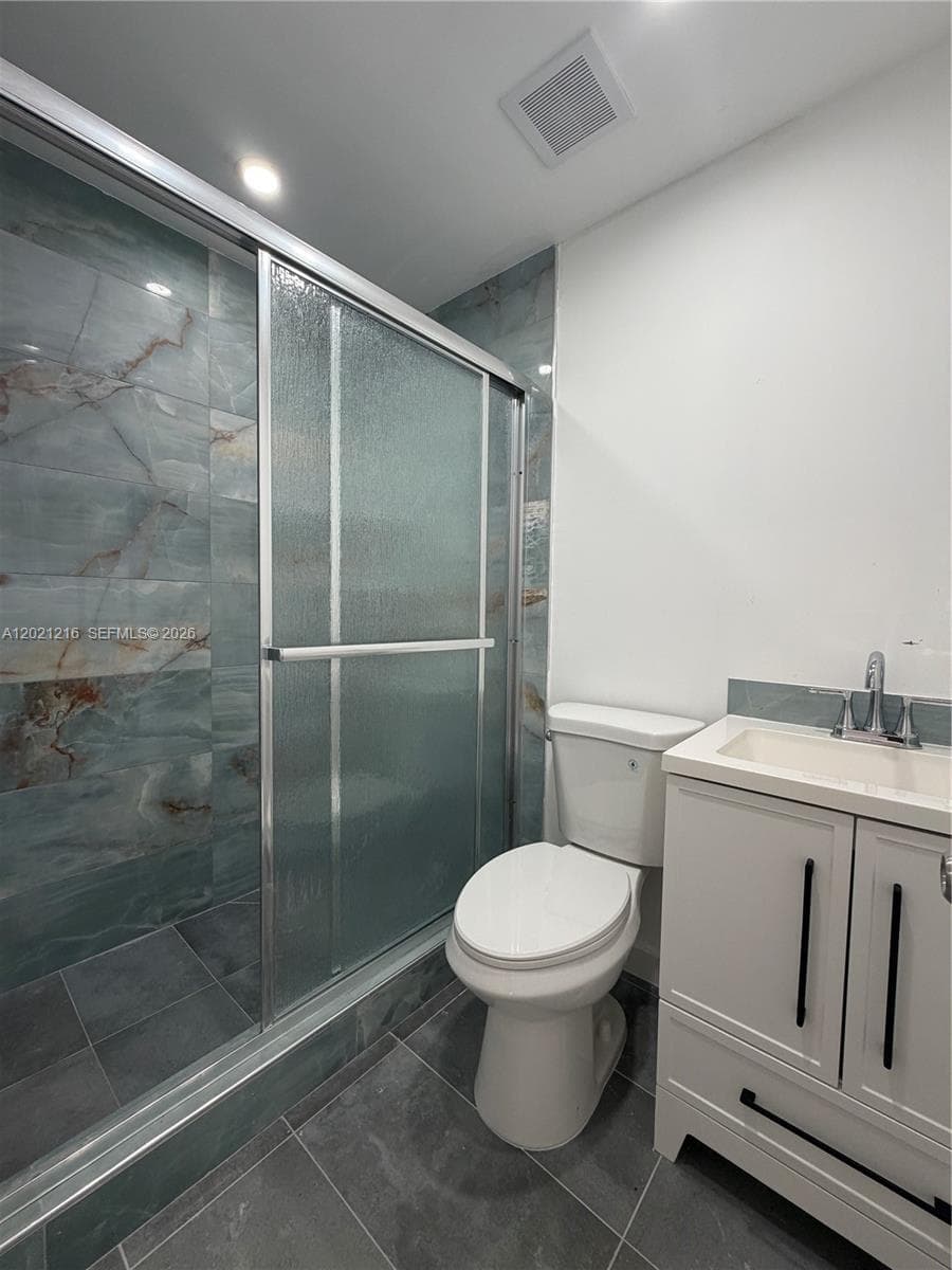 Walk-in shower with textured sliding glass doors and large-format decorative wall tile, vanity cabinet featuring matte black hardware, integrated sink, and charcoal floor tiling