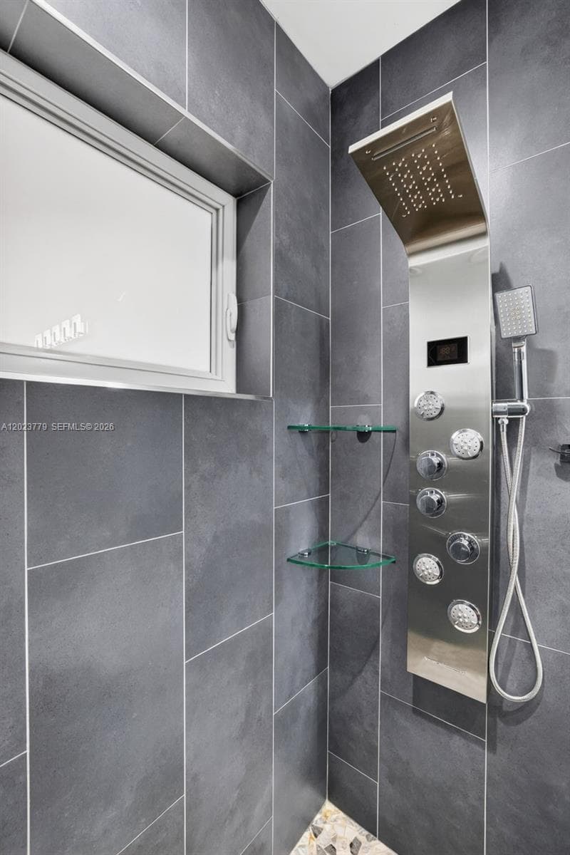Guest bathroom w/ river rock look shower floor, frameless glass shower enclosure, floor to ceiling tile in shower, backlit mirror, solid surface counter and upgraded floor and vanity, w/ multifunction shower head