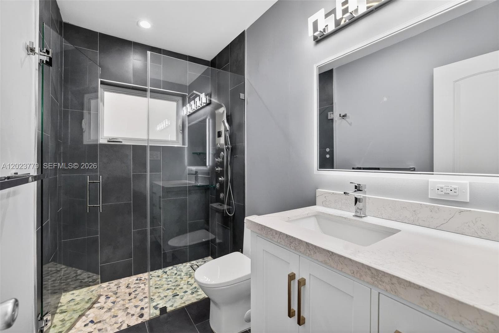 Guest bathroom w/ river rock look shower floor, frameless glass shower enclosure, floor to ceiling tile in shower, backlit mirror, solid surface counter and upgraded floor and vanity, w/ multifunction shower head