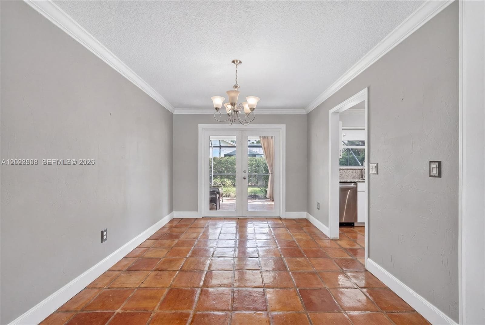 Terra cotta tile flooring, crown molding, multi-light chandelier, and glass-paneled double doors