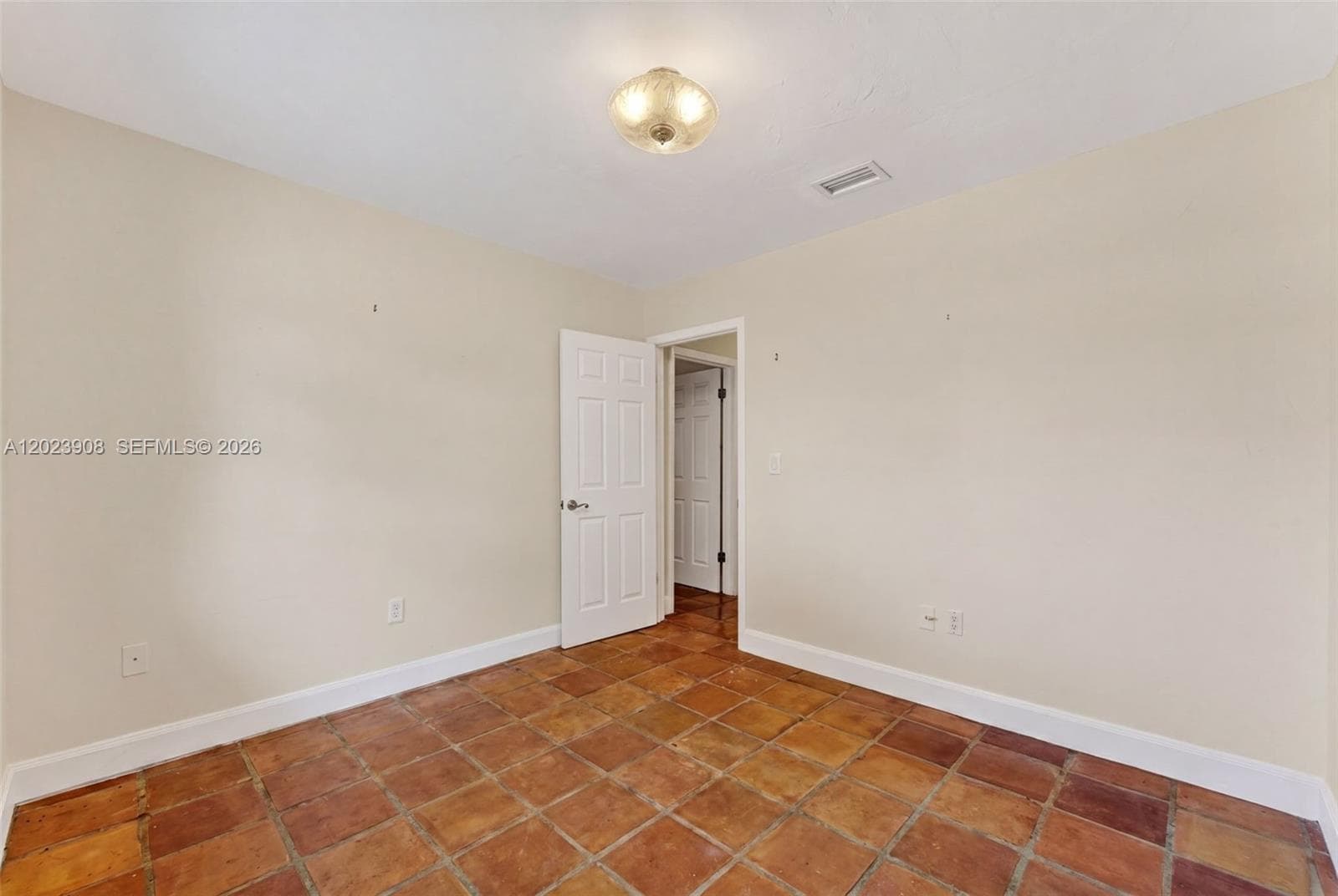 Neutral-toned interior space featuring terracotta tile flooring, six-panel interior doors, and a decorative flush-mount ceiling light fixture