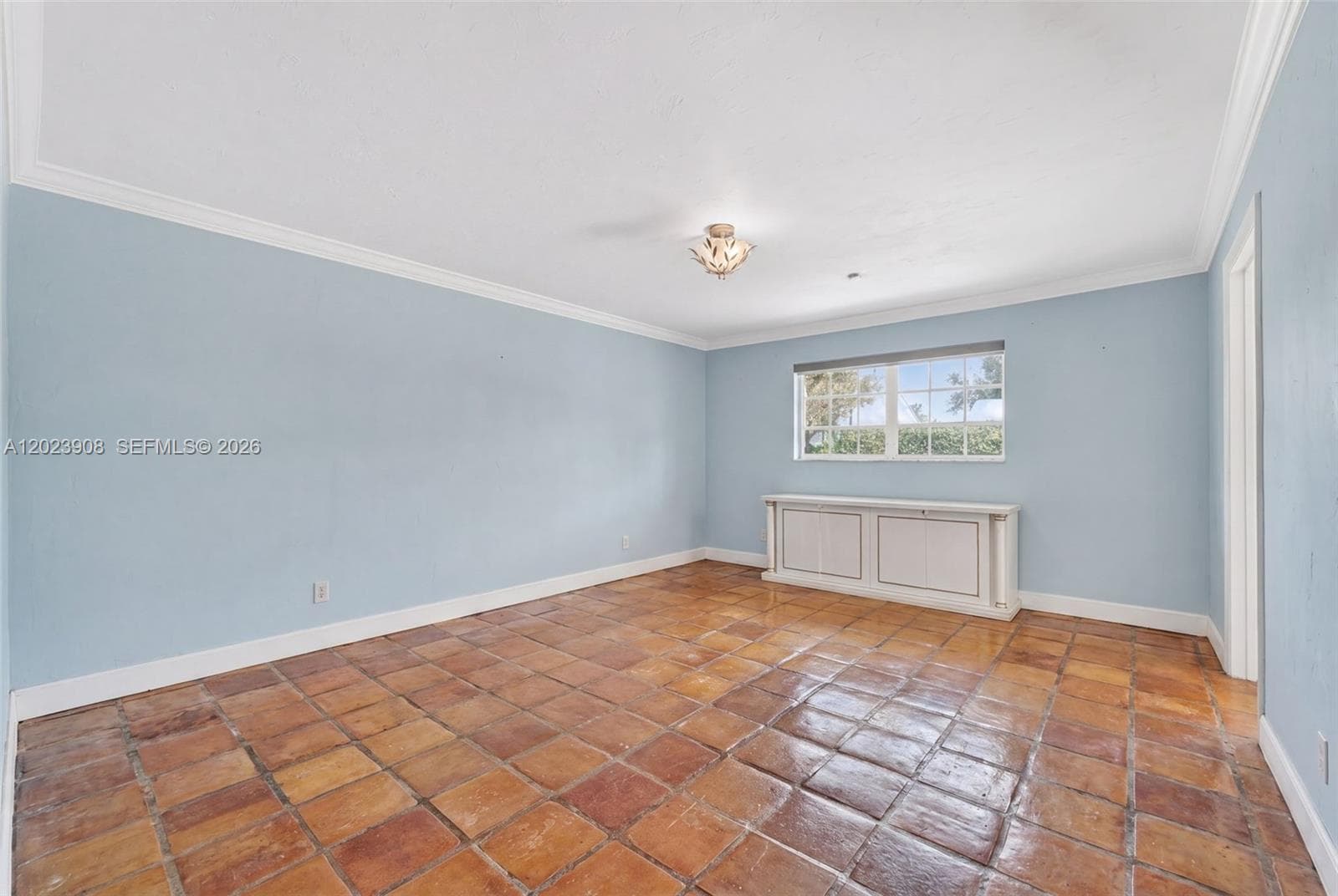 Neutral-toned room featuring terra-cotta tile flooring, crown molding, a built-in cabinetry unit, and a multi-pane window