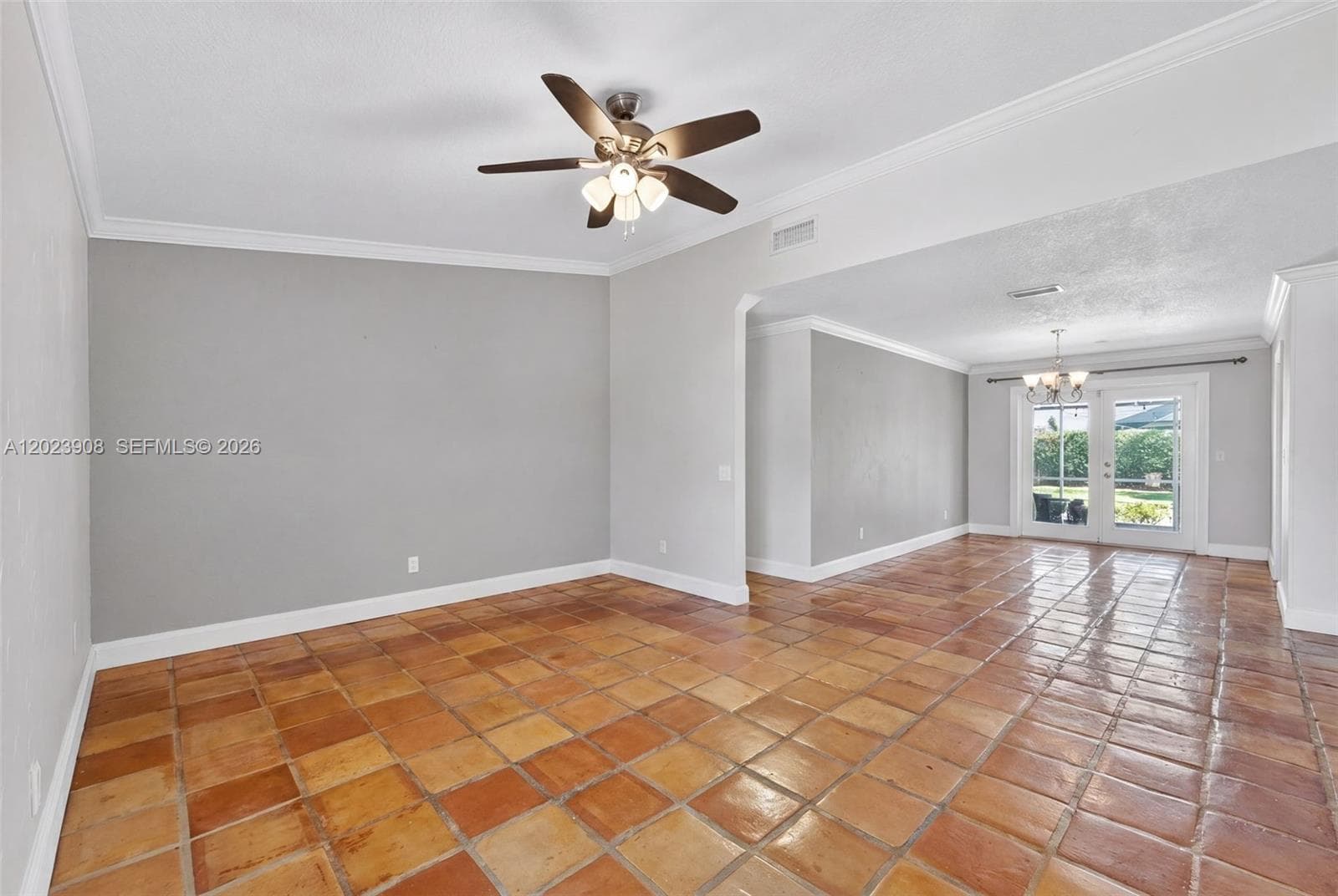 Terracotta tile flooring, multi-light ceiling fan, crown molding, and glass-paned double doors