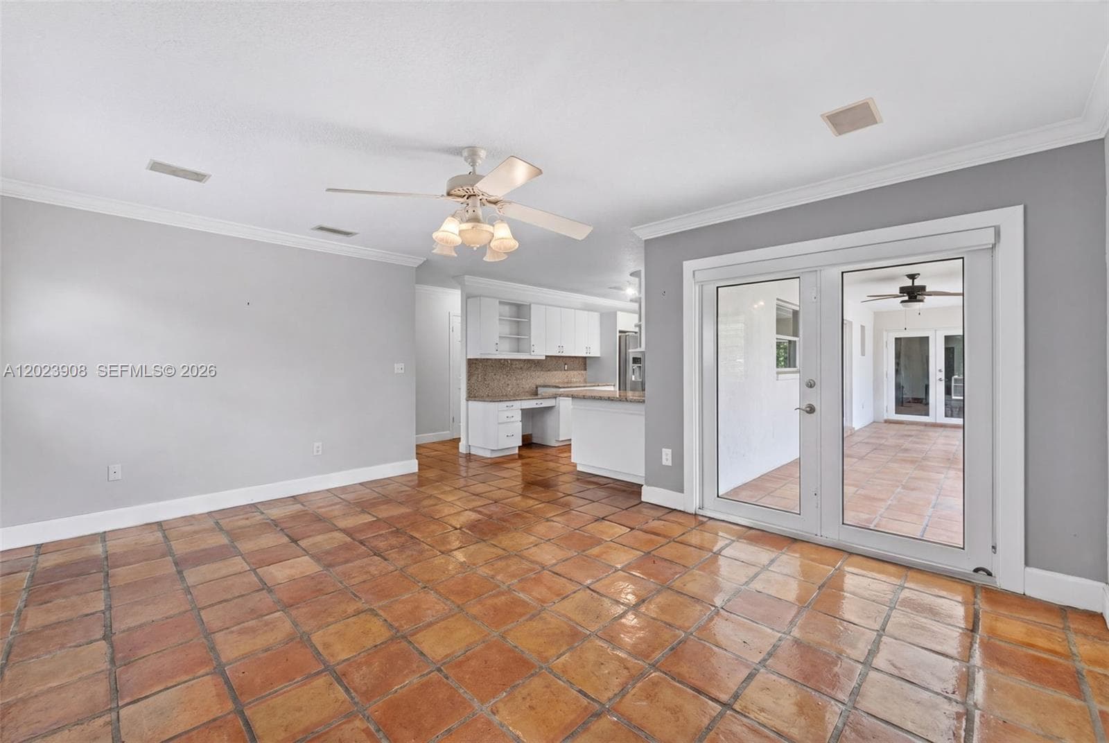 Interior space featuring terra-cotta tile flooring, crown molding, a central ceiling fan with integrated lighting, and glass paneled exterior doors