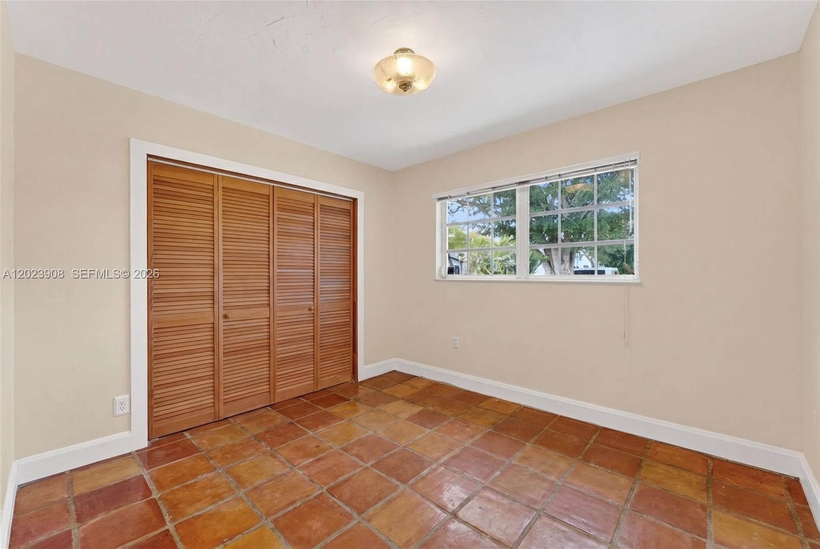 Room featuring terracotta tile flooring, louvered wood-finish closet doors, and a double-pane window