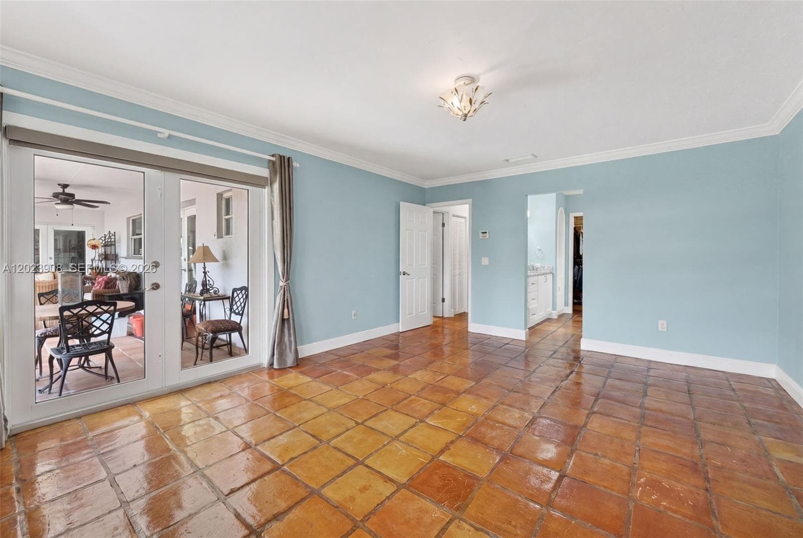 Terra-cotta tile flooring, crown molding, and glass-paned French doors with integrated hardware