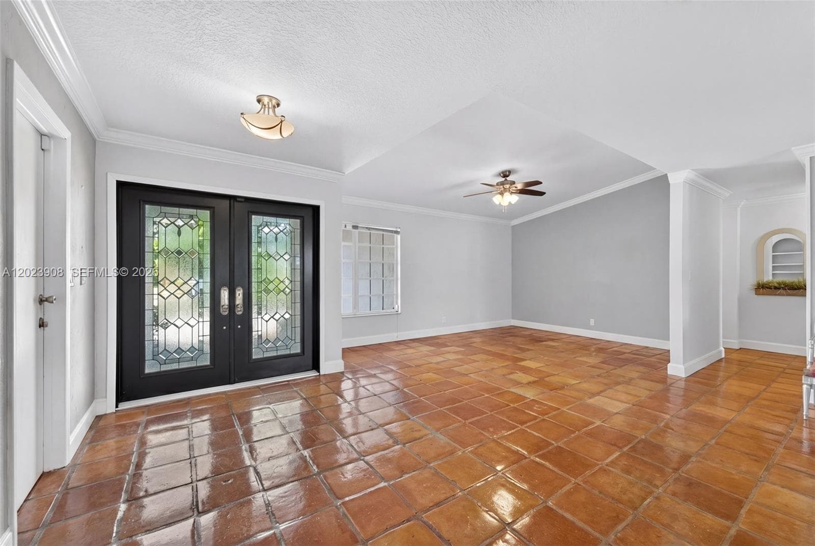 Double front entry doors featuring decorative glass inserts, terracotta-style ceramic tile flooring, recessed ceiling lighting, a ceiling fan with integrated light fixture, and arched wall niche