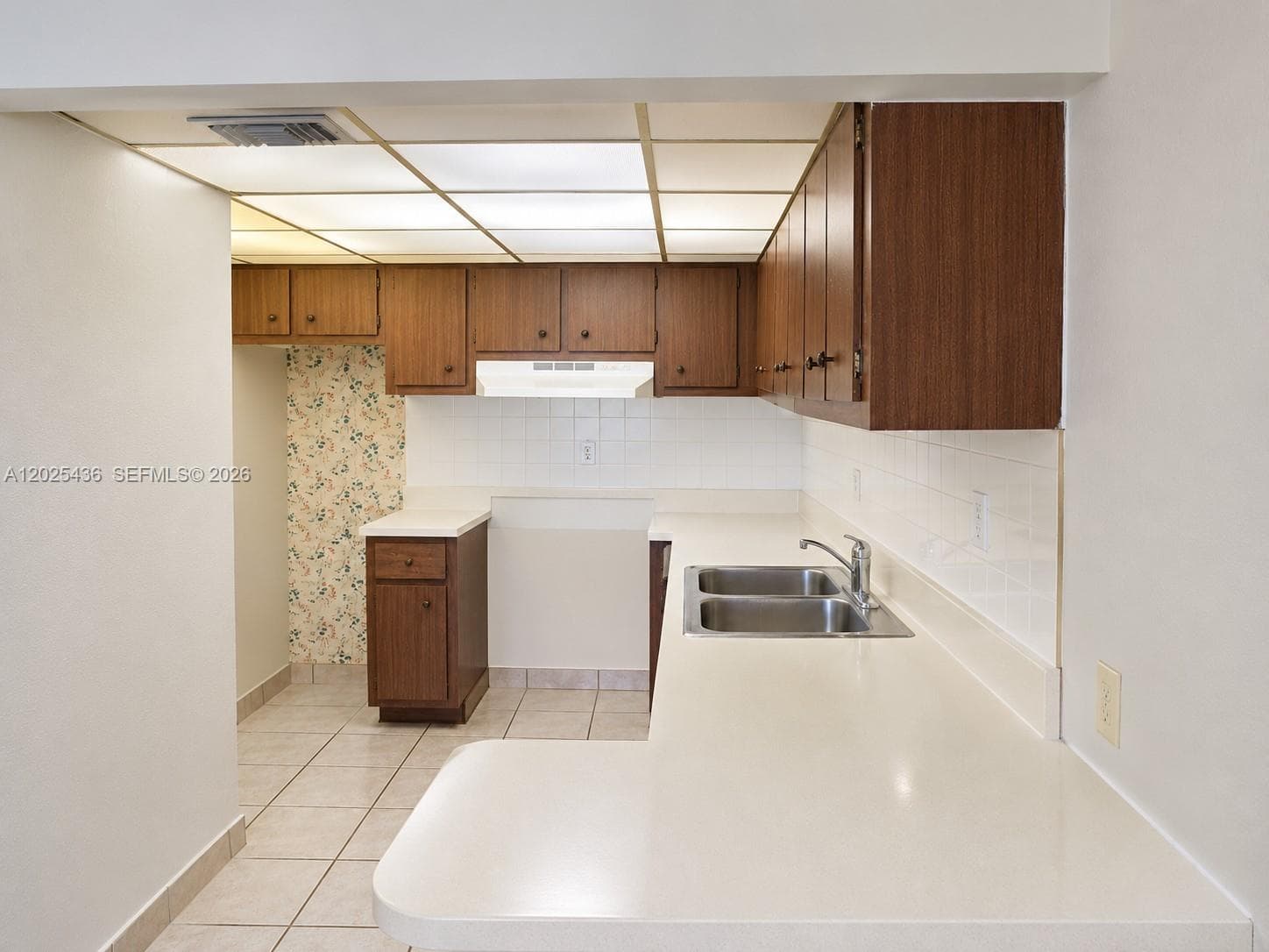 Kitchen featuring solid-wood cabinetry, white tile backsplash, double-basin stainless steel sink, and ceramic tile flooring
