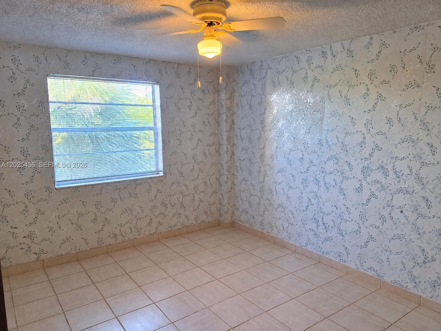 Interior space featuring neutral square floor tiles, patterned wall coverings, a dual-pane horizontal sliding window, and a ceiling-mounted light fixture with a multi-blade fan