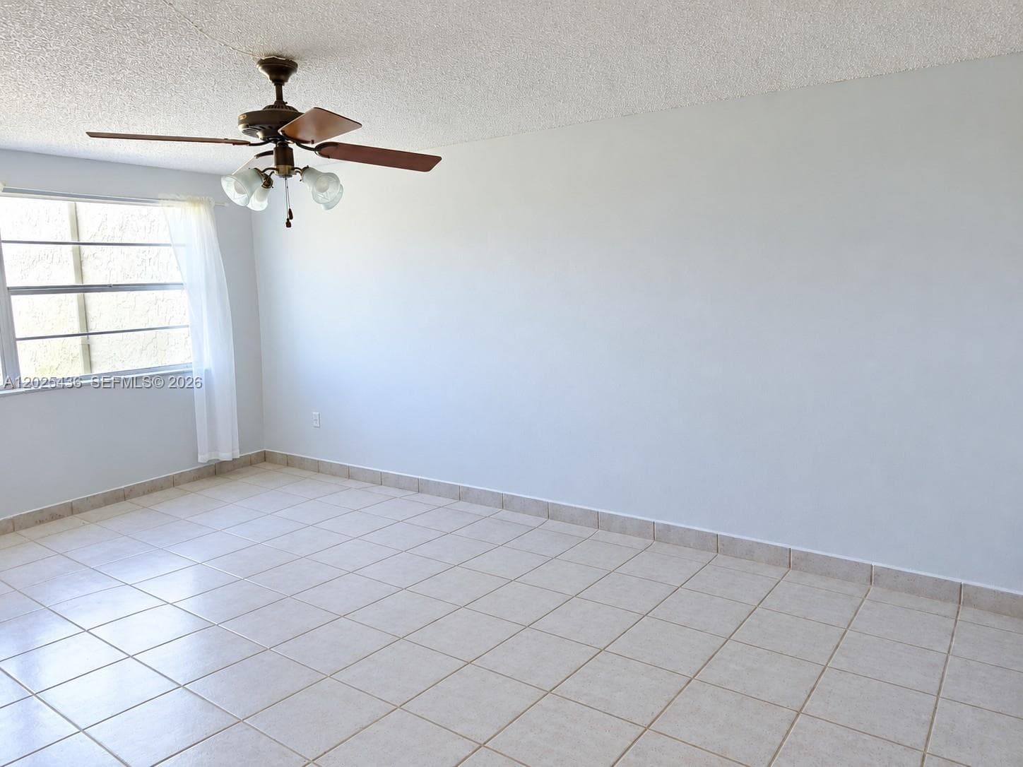 Empty-Interior space featuring large-format tile flooring, textured ceiling finish, and a ceiling fan with integrated multi-light fixture