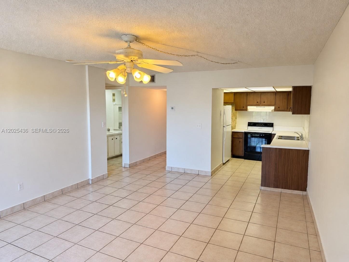 Empty- tile flooring, ceiling fan with integrated lighting, kitchen featuring wood-finish cabinetry, white countertops, and black built-in oven