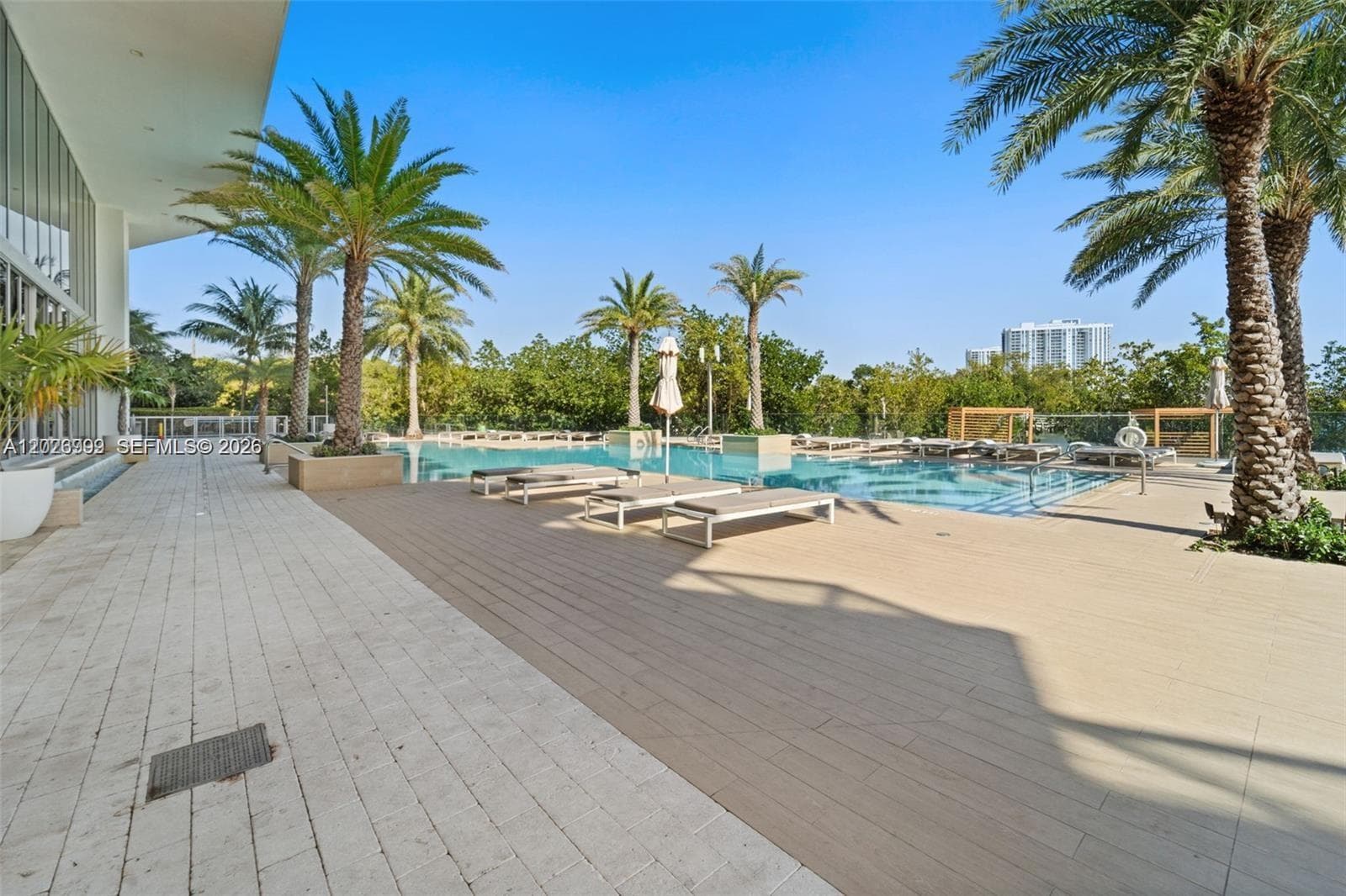 Covered cabana-style seating and an open terrace create a comfortable outdoor lounge area. Lush landscaping and shaded seating offer an inviting setting for relaxing outdoors.