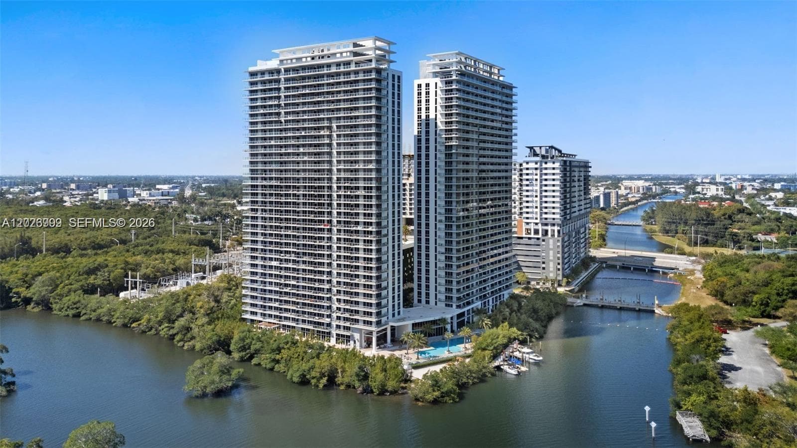 The balcony captures wide water views with surrounding greenery, boats, and the city skyline beyond. Glass railings keep the outlook open and unobstructed.