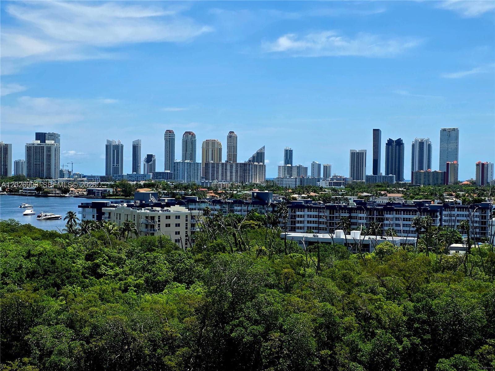 Wide water views stretch over the surrounding greenery, with skyline views visible in the distance. The elevated perspective highlights the property’s scenic waterfront setting.