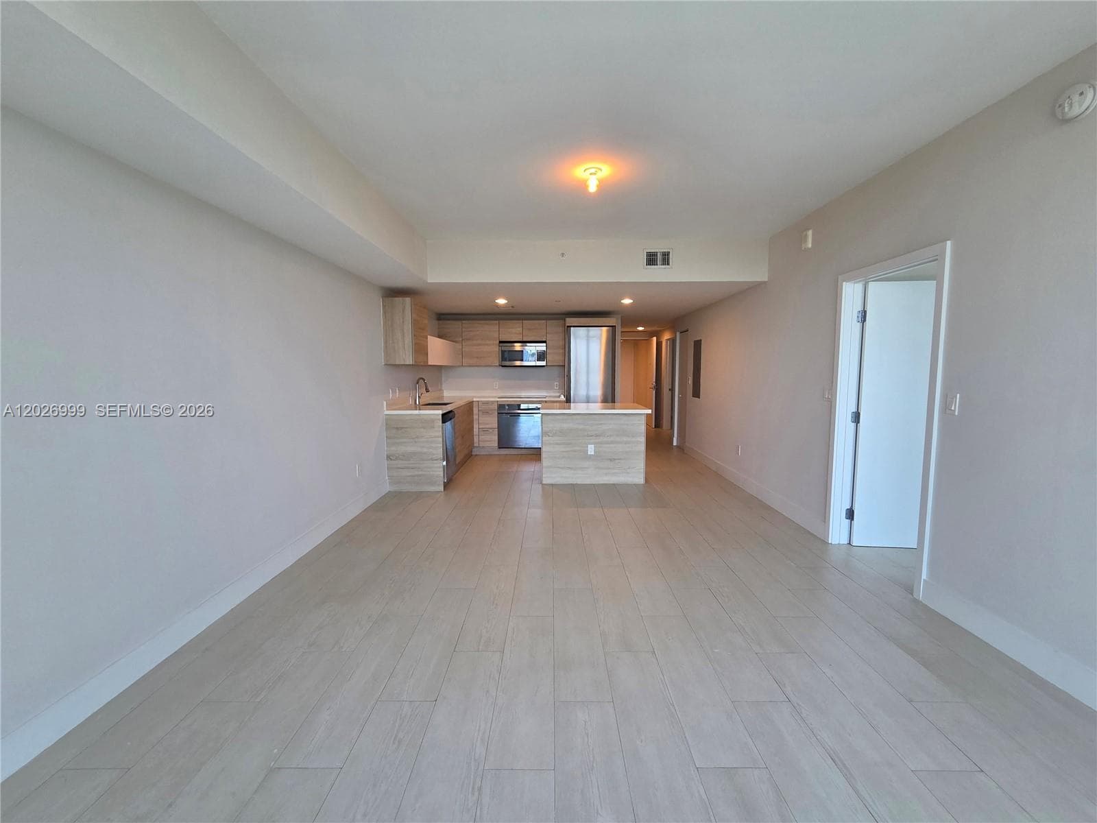 The open kitchen features light wood cabinetry, quartz-style countertops, stainless steel appliances, and a center island that connects easily to the living area.