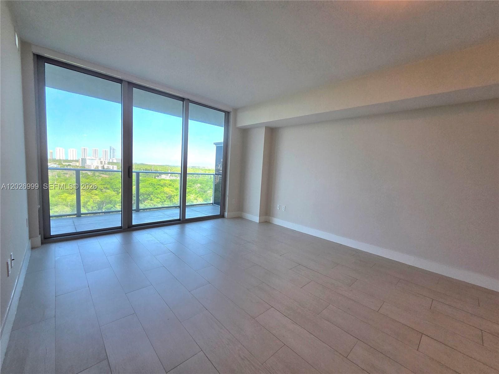 The living room offers generous wall space and a streamlined layout, with natural light entering through the full-height balcony doors.
