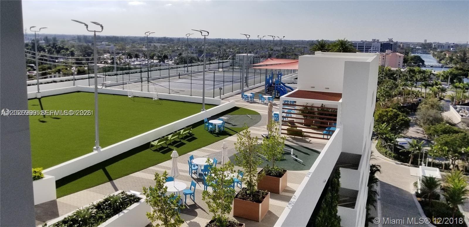 The open-air amenity terrace features lounge seating, dining tables, shaded gathering areas, and turf spaces for relaxed outdoor enjoyment.