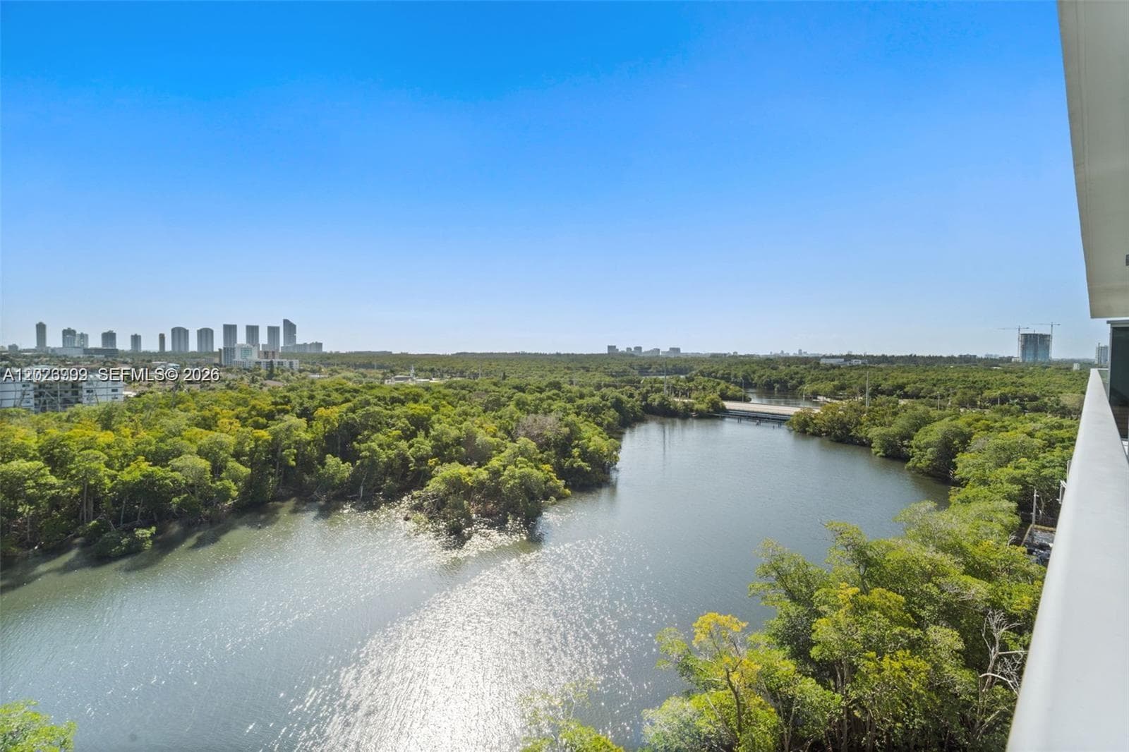 A spacious private balcony extends the living area outdoors, showcasing glass railings, tile flooring, and expansive water and greenery views.