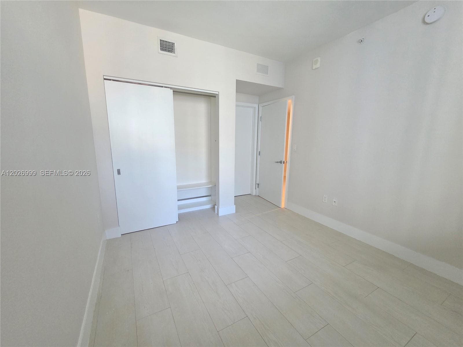 Floor-to-ceiling sliding glass doors open to a private balcony, bringing in natural light and a green treetop outlook.