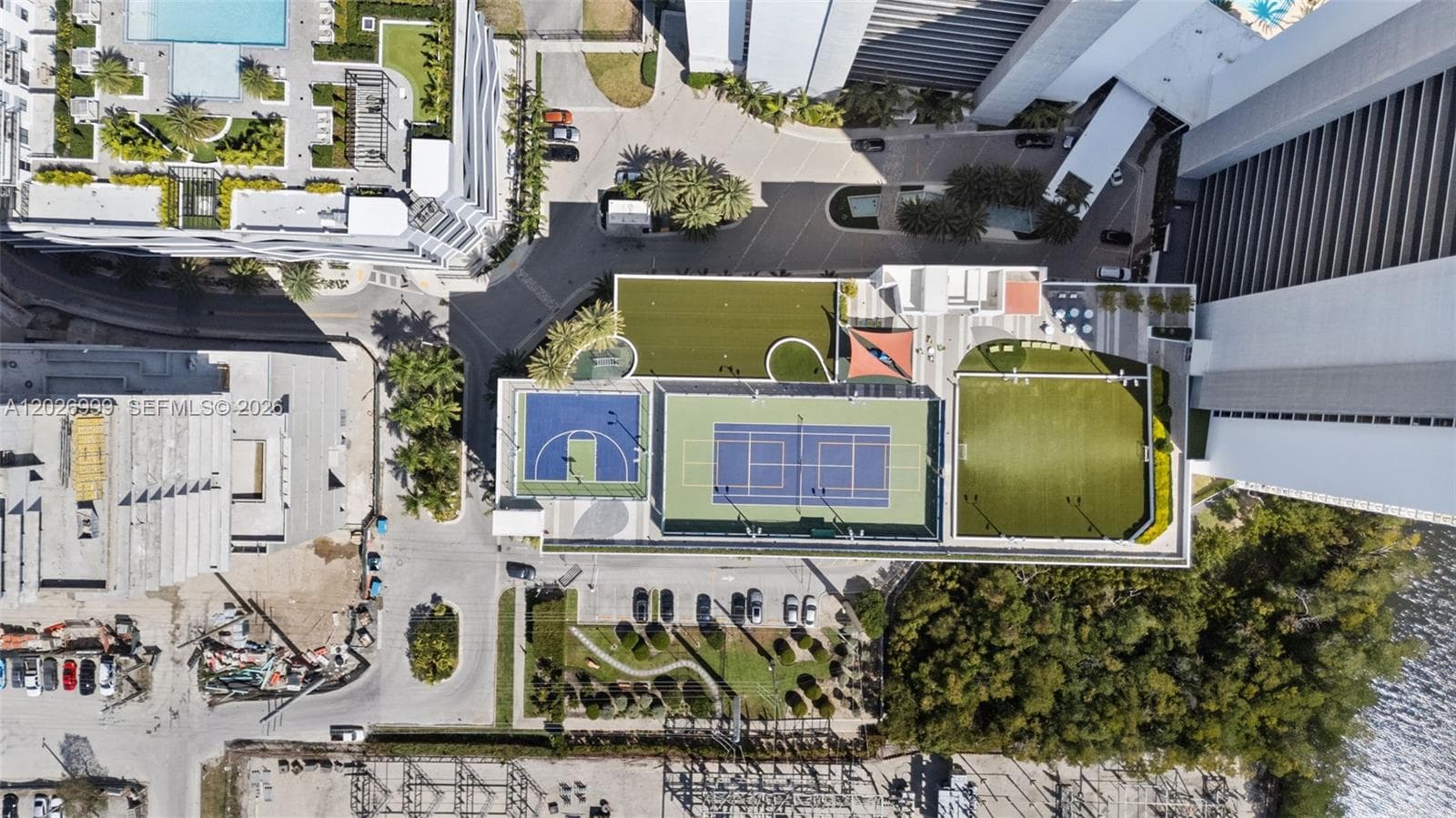 An elevated exterior view highlights the waterfront setting, with the residence positioned near surrounding waterways, greenery, and nearby high-rise buildings.