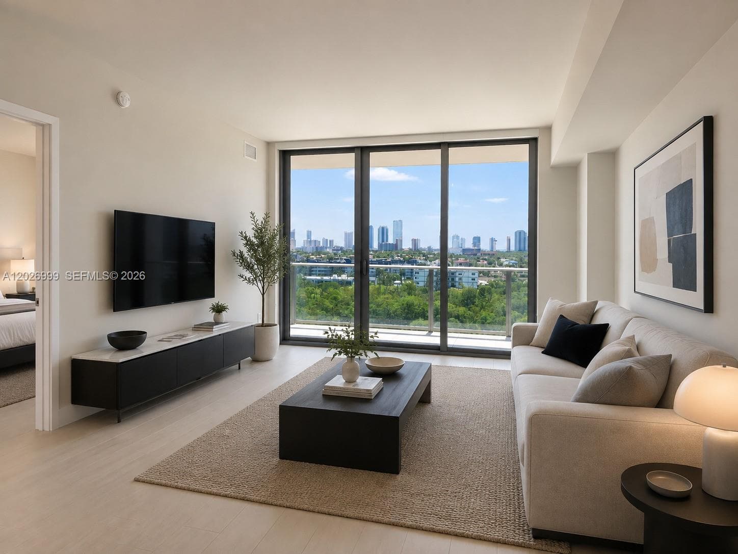 A bright open living area with light tile flooring, floor-to-ceiling sliding glass doors, and direct balcony access showcasing greenery, water, and skyline views.