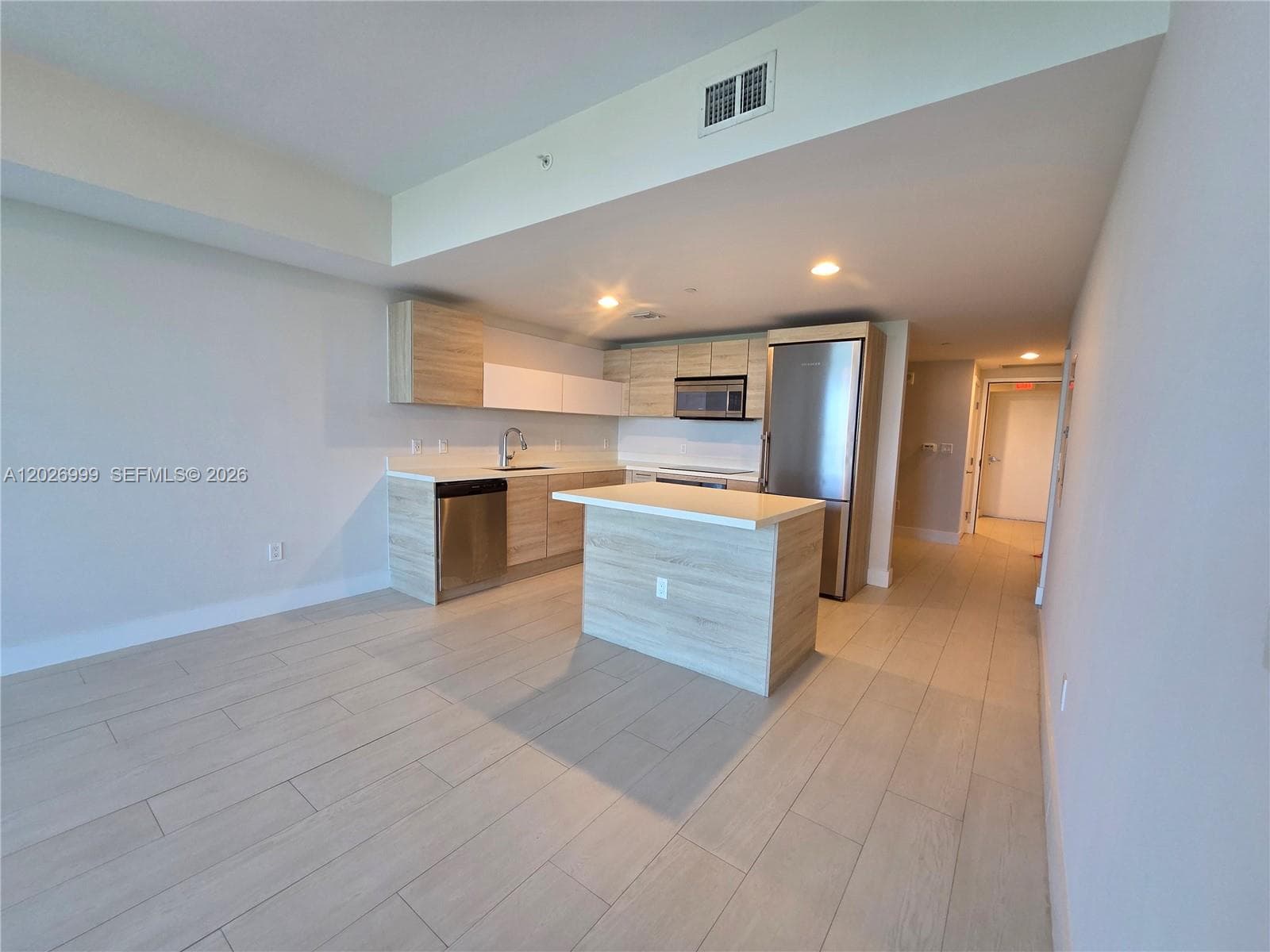 The entry opens into a modern kitchen and living space with wood-look cabinetry, a central island, and floor-to-ceiling glass framing the view beyond.